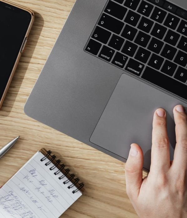 Crop person working on laptop at table with smartphone and notepad