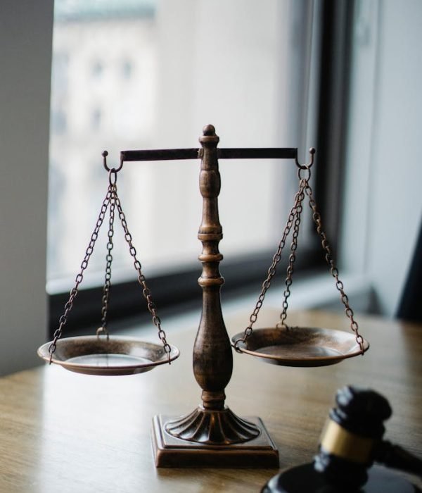 Decorative judgement scale and gavel placed on desk in light lawyer office against window